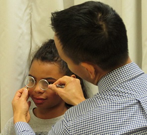 Young girl getting her eyes checked by a male holding small lenses in front of her eyes.