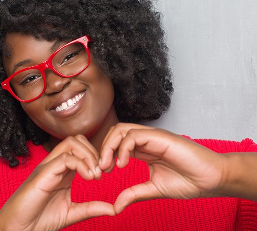 Pearle Vision: Woman wearing red glasses holding up a heart with her hand