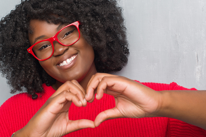 Woman wearing red glasses holding up a heart with her hand