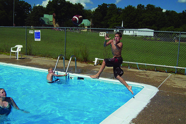 Boy jumping into a pool while simultaneously catching a football. 