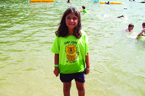 Young girl wearing a camp lions shirt and swimming in the lake.