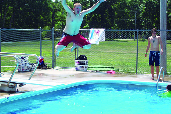 Male camper jumping into a swimming pool on a diving board.