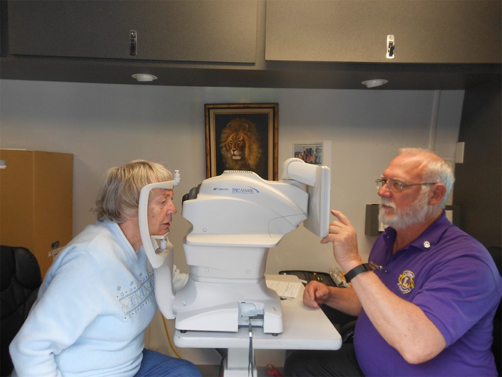 An elderly woman getting her eyes checked at a mobile screening unit for retinal eye diseases.