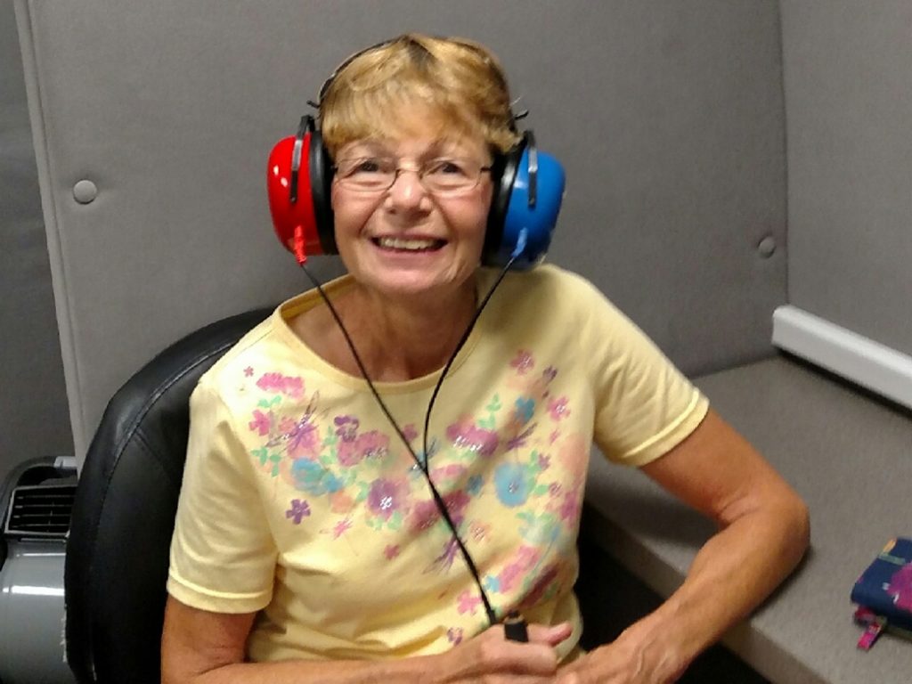 Elderly woman smiling wearing blue and red headphones while getting her hearing checked.